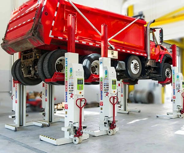 Red truck elevated on white hydraulic lifts in a workshop.